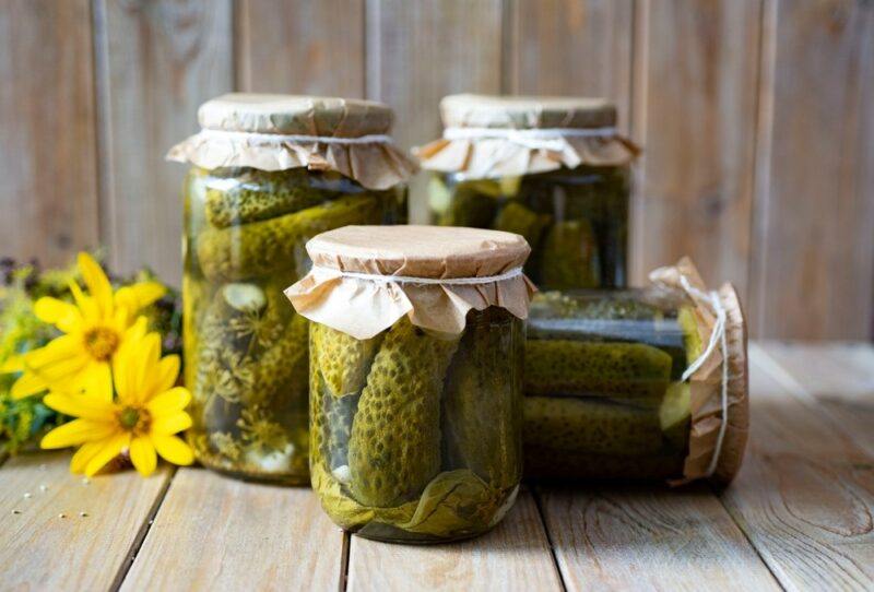 Three sealed glass jars of pickles standing upright and one lying down