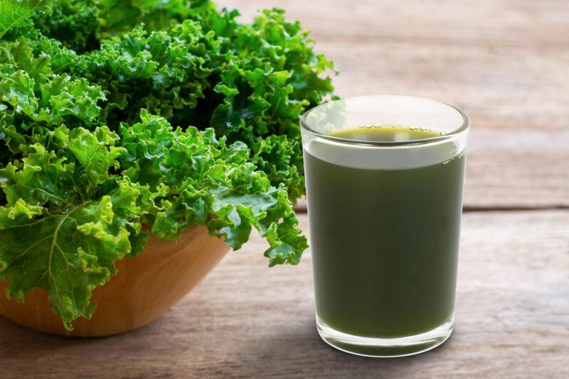 on a wooden surface is a bowl full of fresh kale and a glass full off kale juice