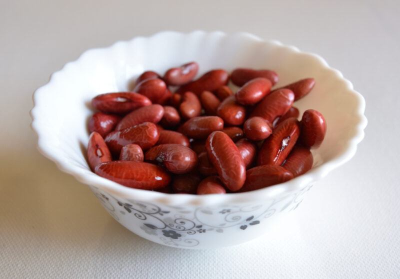 on a white surface is a white ceramic bowl with flower designs full of kidney beans