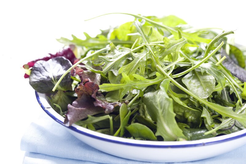 closeup image of a white bowl with blue lining full of leafy greens vegetables, bowl is resting on top of a pale blue table napkin