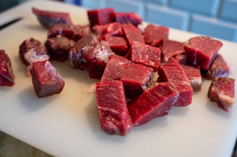 closeup image of cubed red meat on a white plastic chopping board