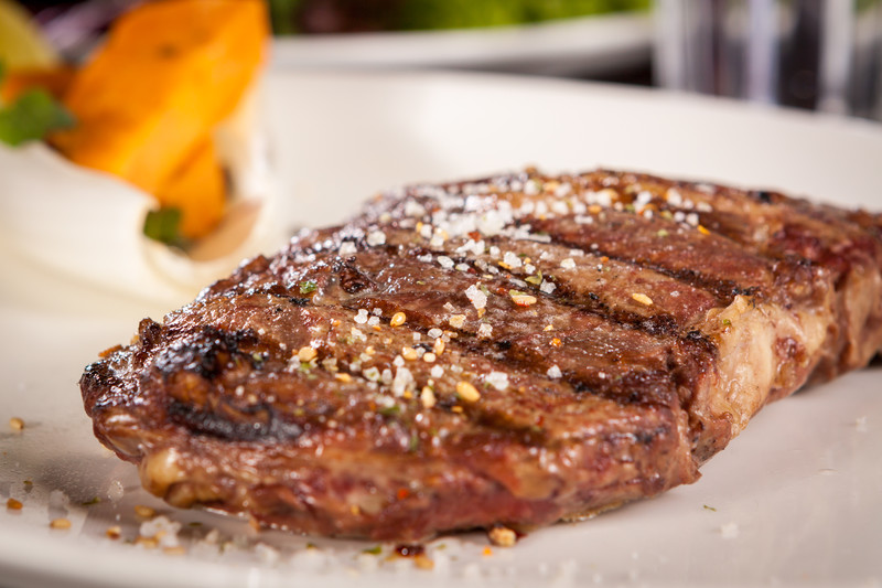 A grilled steak rests on a white plate.