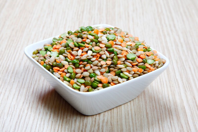 on a pale wooden surface is a white square-shaped bowl full of legumes