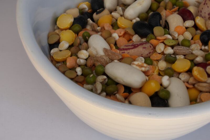 partial image of a white bowl full of different types of legumes resting on white surface