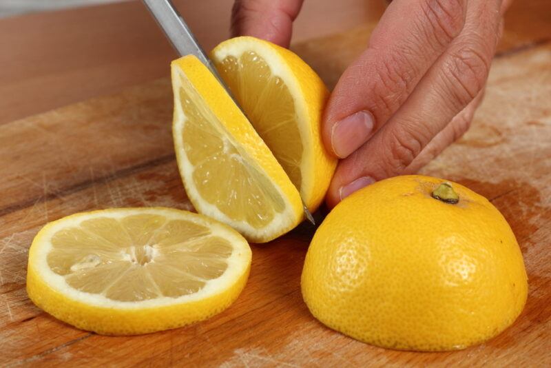 on a wooden chopping board is a hand slicing fresh lemon