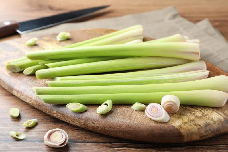 lemongrass stalks on a round wooden chopping board with a knife beside it and loose cut lemongrass