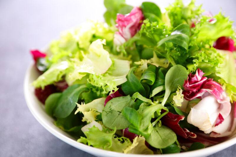 on a grey surface is a closeup image of a bowl full of different types of lettuces