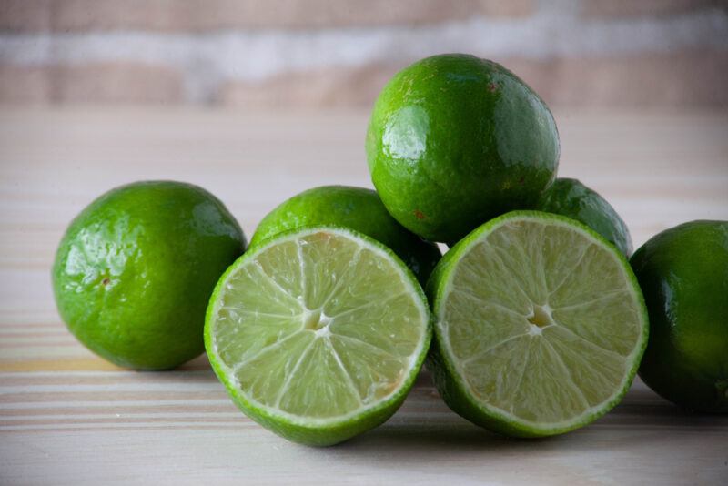 on a wooden surface is a plie of limes with one cut in halves