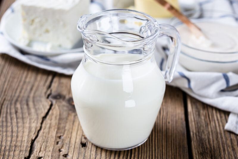 on a rustic looking wooden surface is a spread of low fat dairy products including a jug of low fat milk, yogurt, and cheese