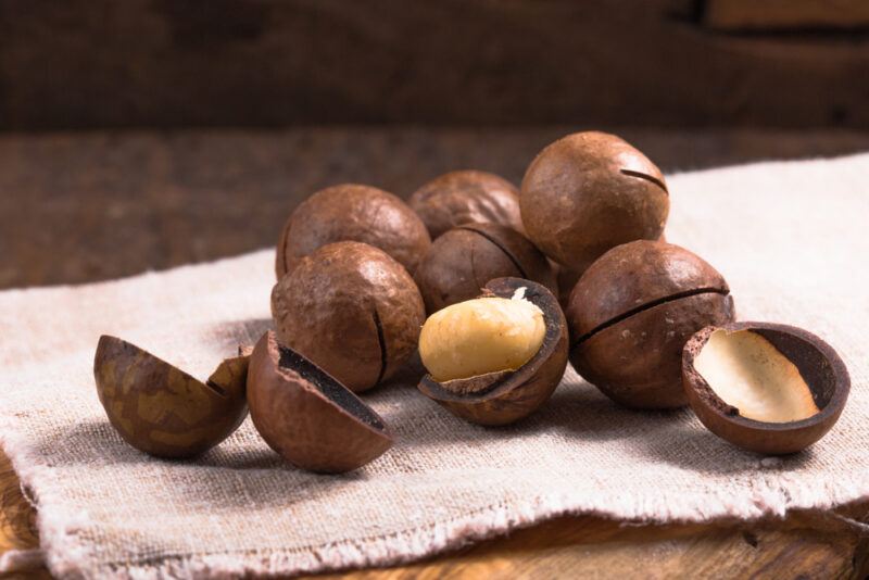 on a wooden surface is a brown cloth with macadamia nuts with a couple of them cracked open