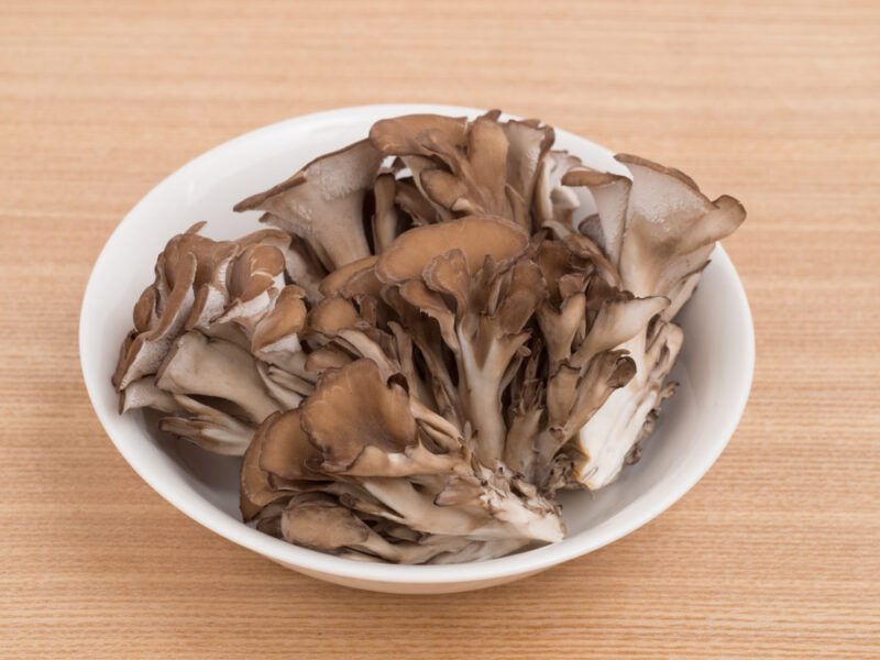 on a wooden surface is a white plate with maitake mushrooms in it