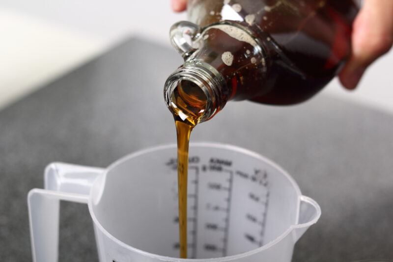 maple syrup being poured into a measuring cup from an amber colored glass jar