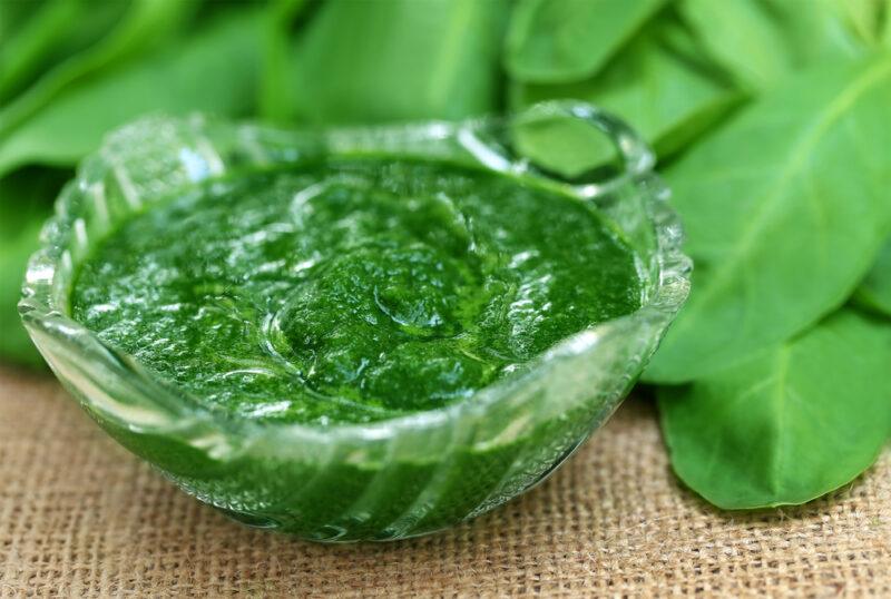 on a burlap table napkin is a clear glass bowl of mashed spinach, at the back are fresh spinach