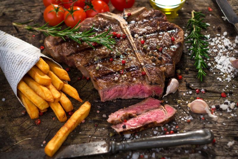 medium rare t-bone steak with french fries and garnishes