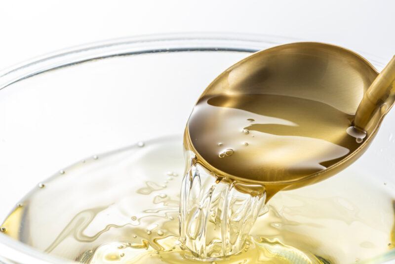 closeup image of a clear glass bowl with mirin and a gold-colored metal scoop