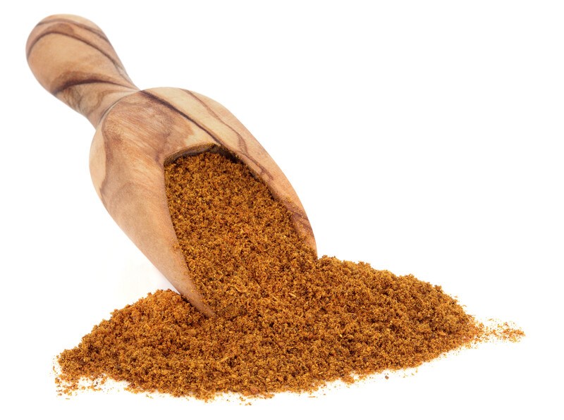 against a white background is a mound of Ras el hanout with a wooden scoop shove in it