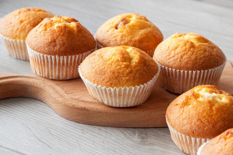 on a wooden surface is a wooden chopping board with muffins