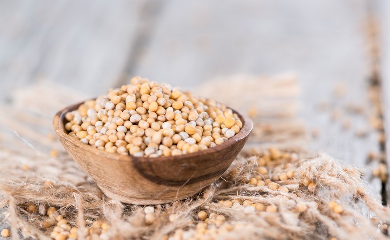 a closeup image of a clay bowl full of mustard seeds resting on a burlap sack with loose mustard seeds on it