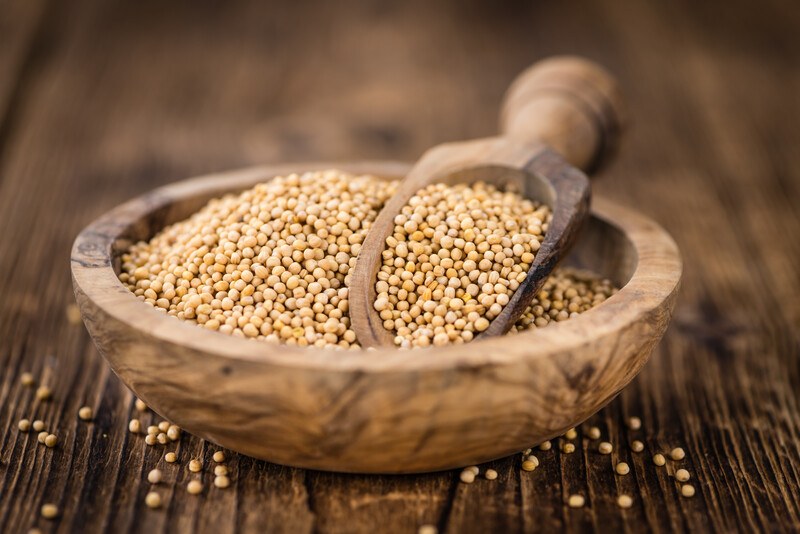 on an aged wooden surface is a wooden bowl full of mustard seeds with wooden scoop in it