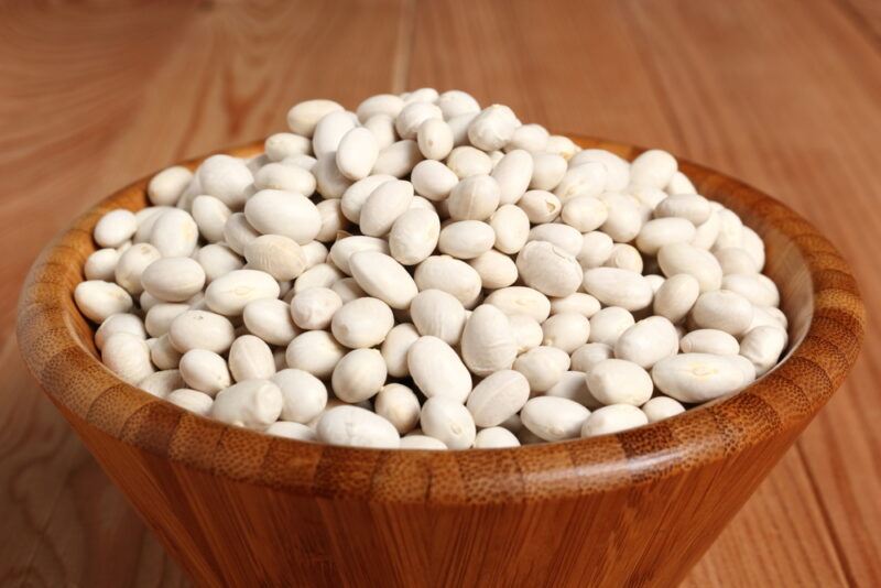 on a wooden surface is a wooden bowl full of navy beans