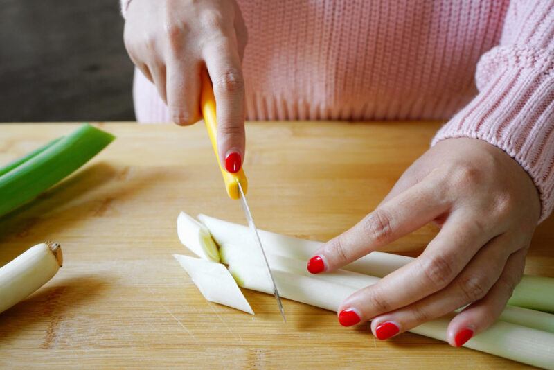 hands with red nail polish cutting negi on a wooden surface