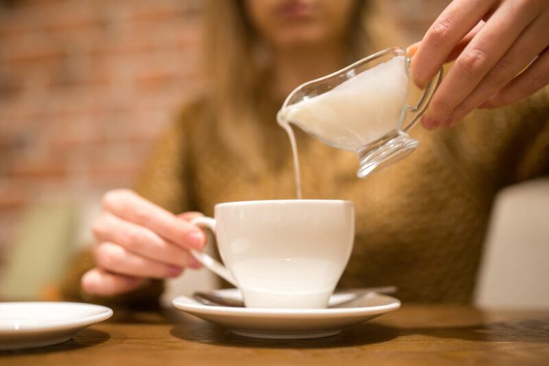 a partial image of a woman pouring non dairy creamer in her coffee