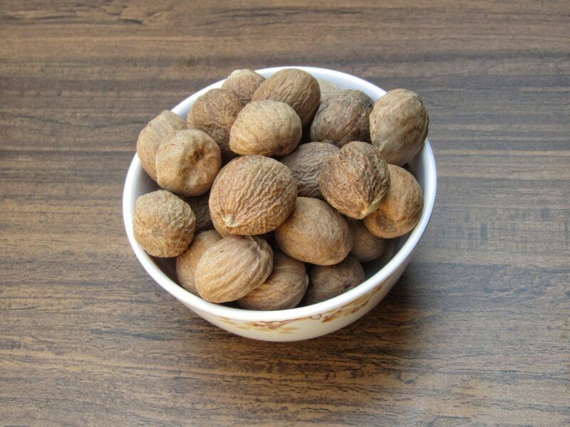 on a wooden surface is a white bowl with whole nutmegs