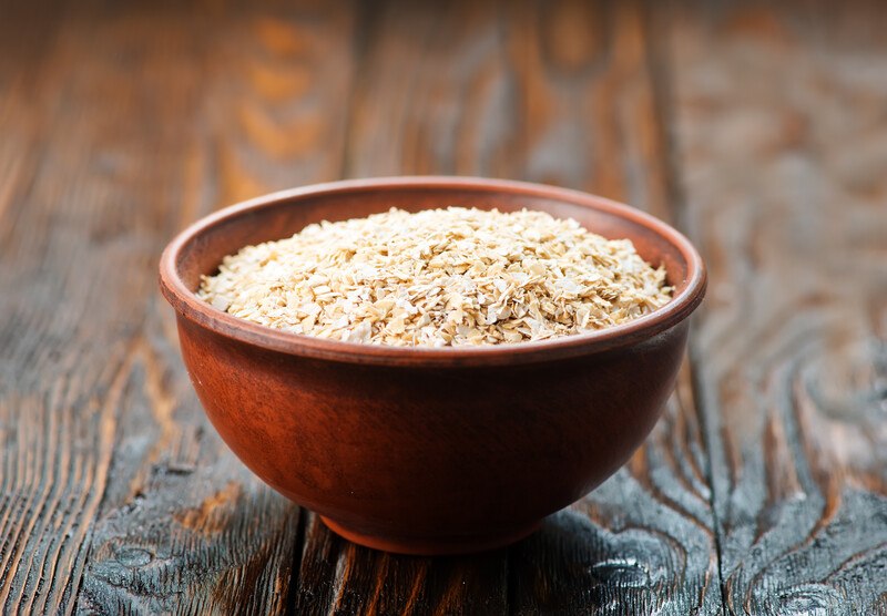 on a dark rustic wooden surface is a brown wooden bowl of oat bran