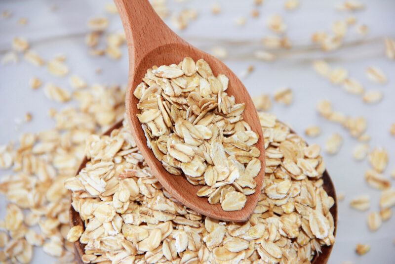 on a wooden surface is a closeup image of a bowl of oatmeal with a wooden spoon over it also filled with oatmeal