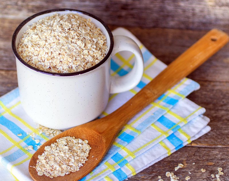 a white mug with blue rim full of oatmeal with a wooden spoon with oatmeal on it, both are resting on a white table napkin with blue and yellow stripes