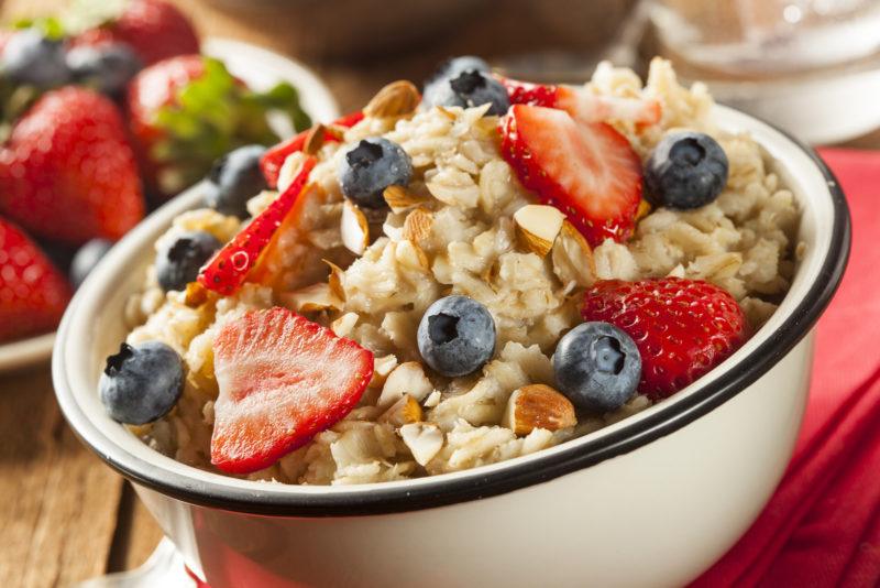 white bowl filled with oats and topped with sliced strawberries, blueberries, and nuts.