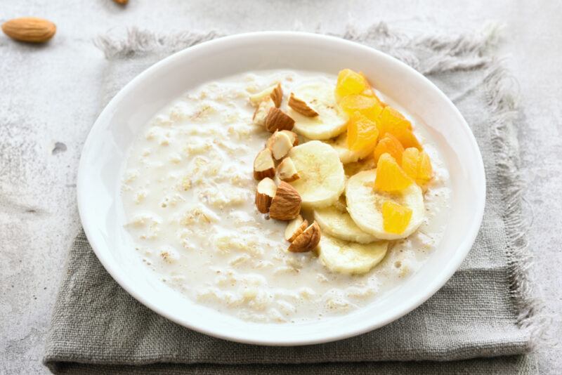 on a light grey table napkin is a dish full of oatmeal with sliced bananas, almonds, and apricots