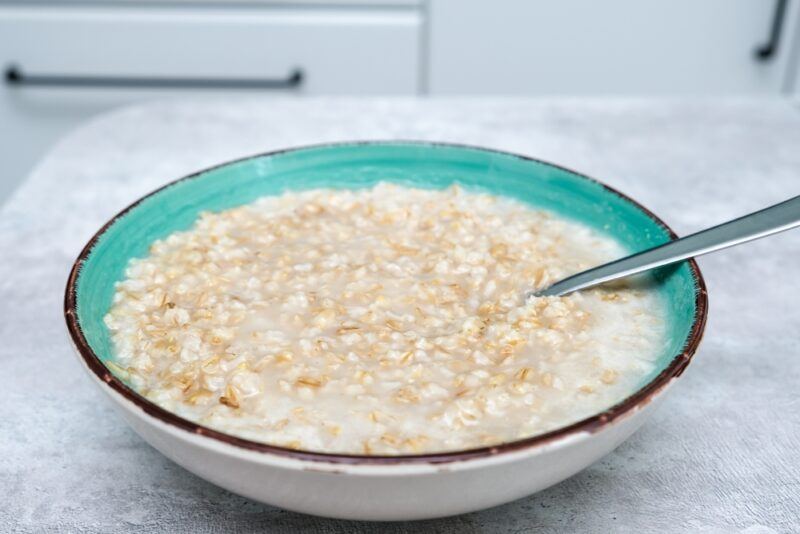 a white and turquoise bowl with brown rim with porridge made from oats, a whole grain