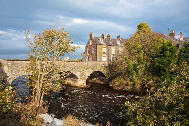 old bushmills irish whiskey distillery next to river with stone bridge