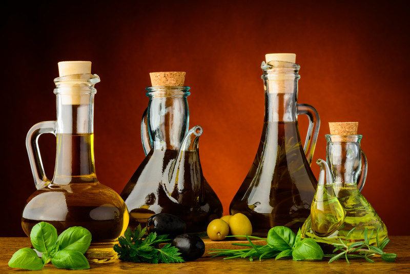 Various bottles and colors of olive oil 
 from an olive oil of the month club. These bottles are on a wooden board with fresh herbs