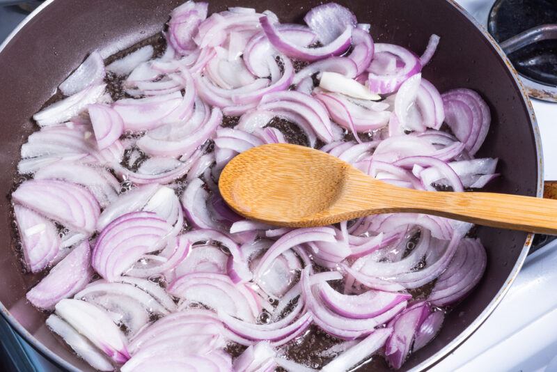 thinly sliced onions being sauteed on a frying pan with a wooden ladle 