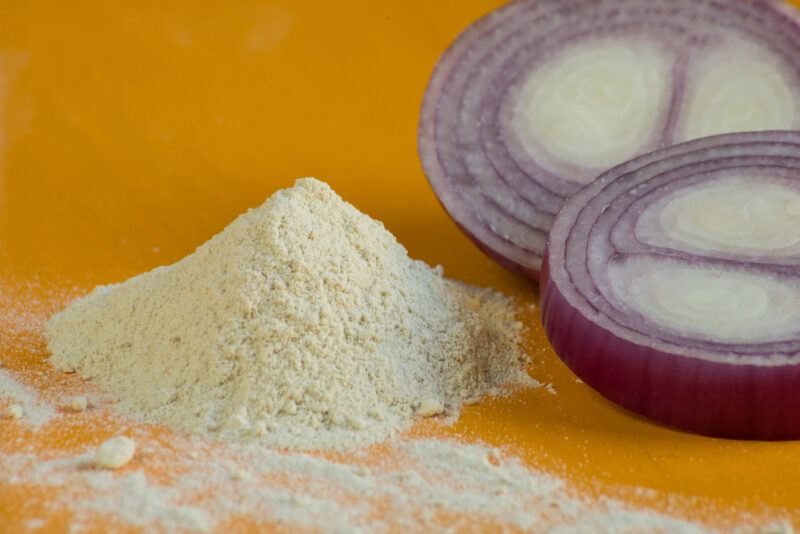 on a yellow surface is a mound of onion powder with sliced red onions beside it