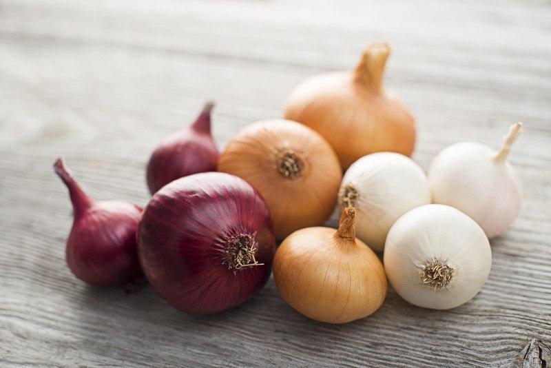 closeup image of different kinds of onions laid out on a wooden surface