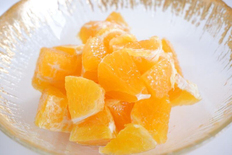 closeup image of a clear glass bowl with orange bits, resting on a white surface