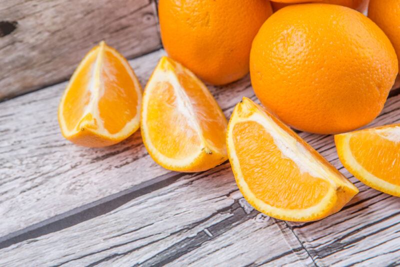 on a rustic looking wooden surface are orange wedges and a couple of whole oranges