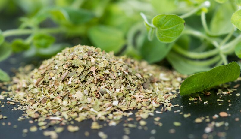 closeup image of dried oregano and fresh oregano leaves on a dark surface