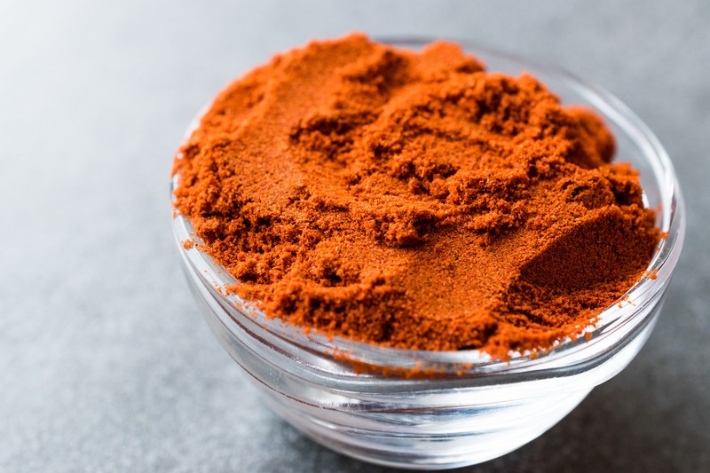 on a grey concrete surface is a closeup image of glass bowl full of paprika powder