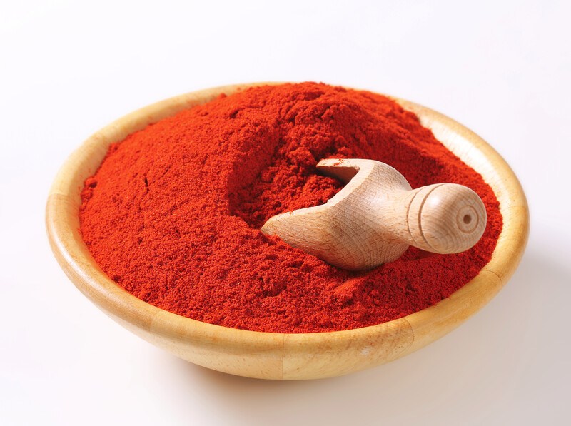 a wooden bowl full of paprika powder with a wooden scoop in it