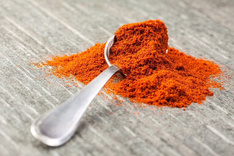 closeup image of a silver spoon full of paprika with some powder spilling over the wooden surface