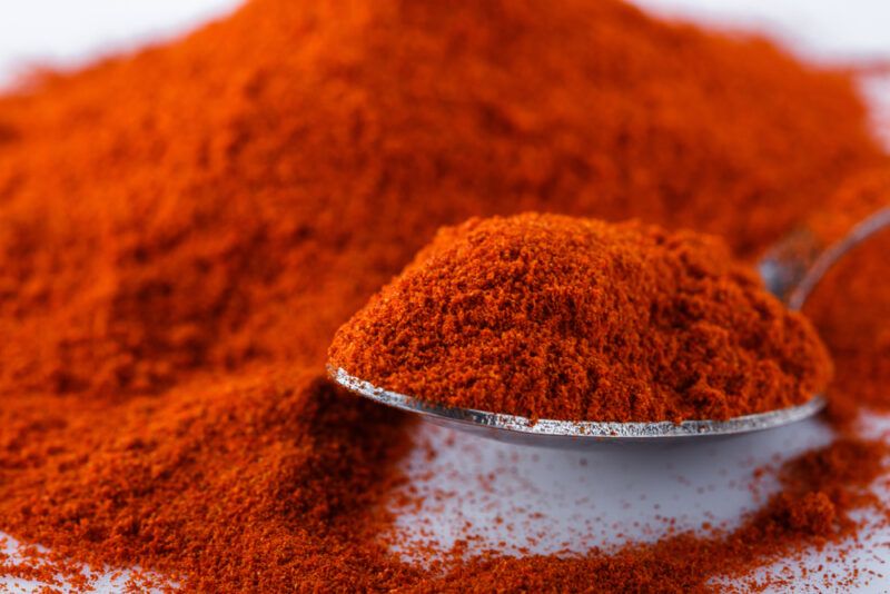 a closeup shot of a mound of paprika powder with a sliver spoon full of paprika powder as well