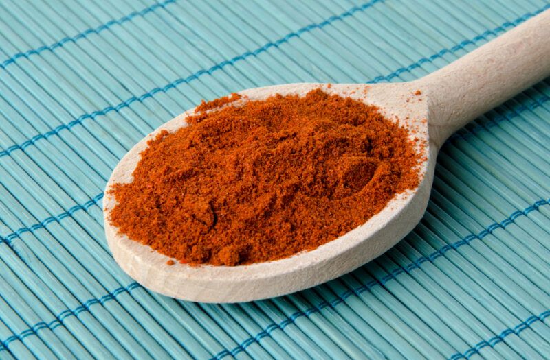 on a blue bamboo table mat is a wooden ladle full of paprika powder