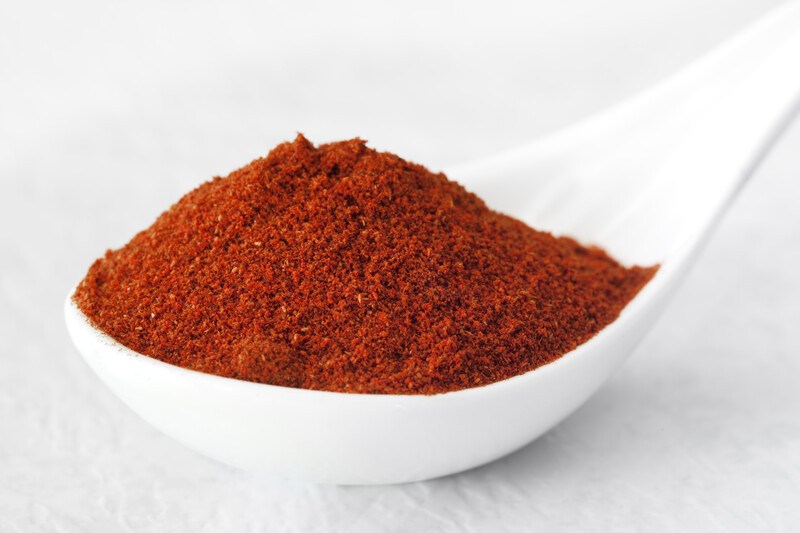 a white porcelain spoon full of paprika powder against a white background