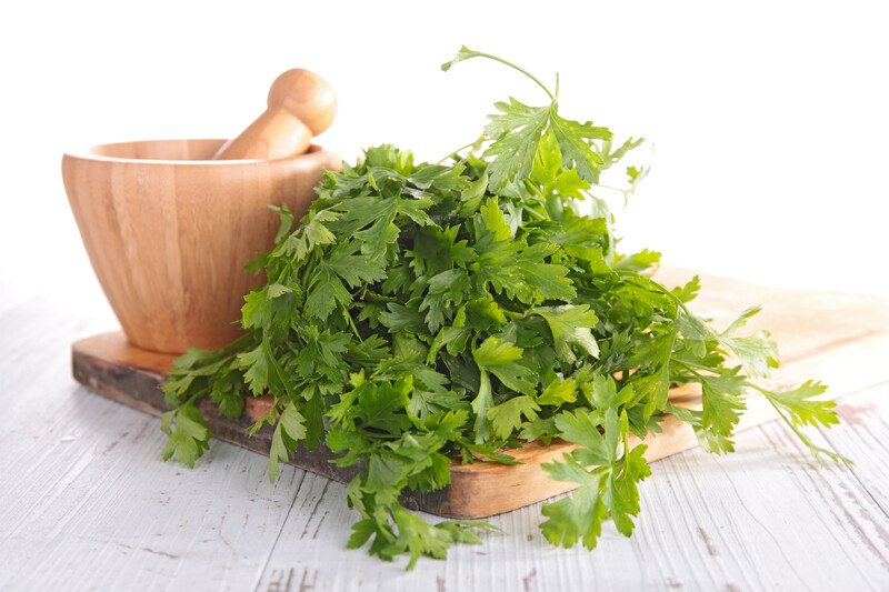 closeup image of a bunch of fresh parsley on a wooden board with a wooden mortar and pestle at the back