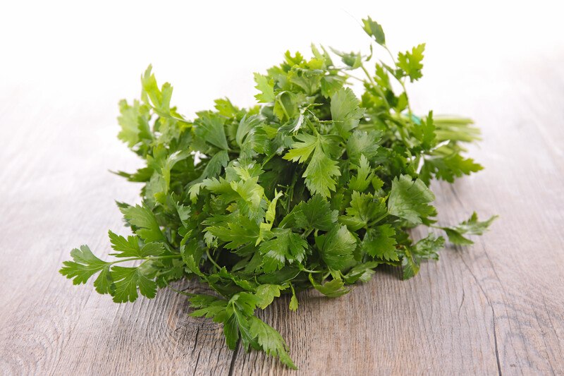 on a wooden surface is a bunch of fresh parsley herbs