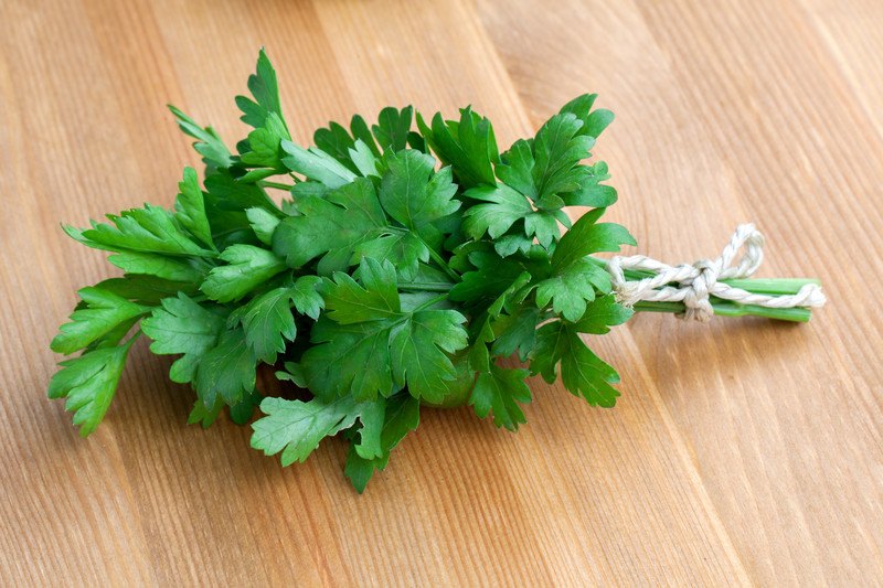 A green bundle of parsley, tied with twine, rests on a wooden tabletop.